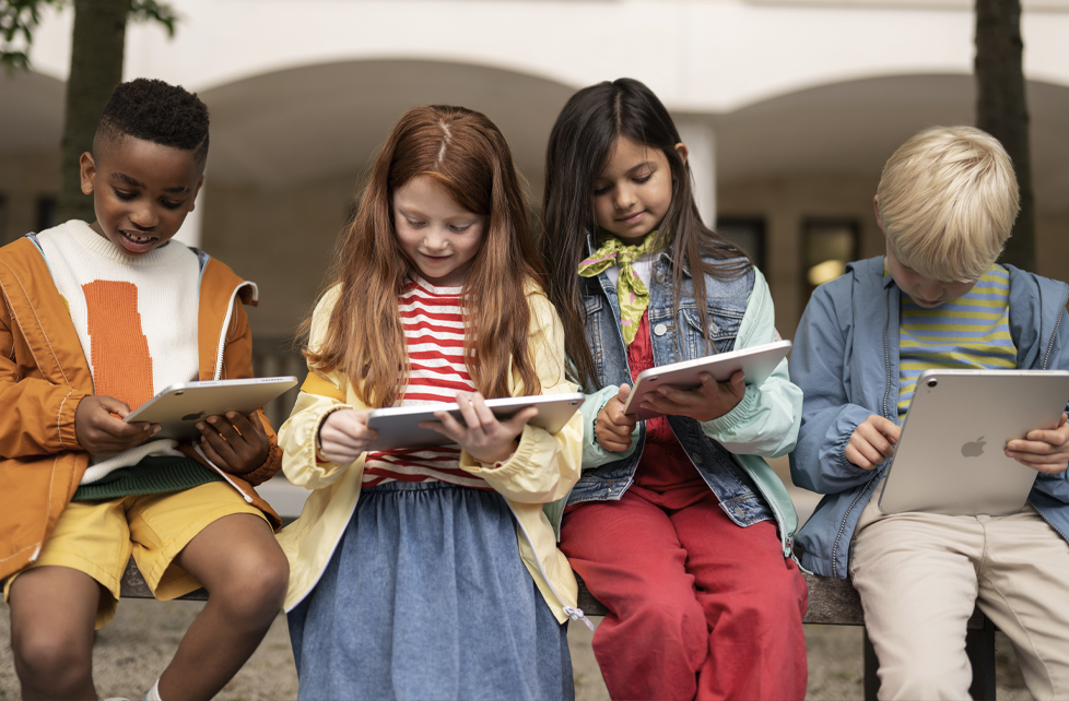 Group of young students using iPads while sitting outside school