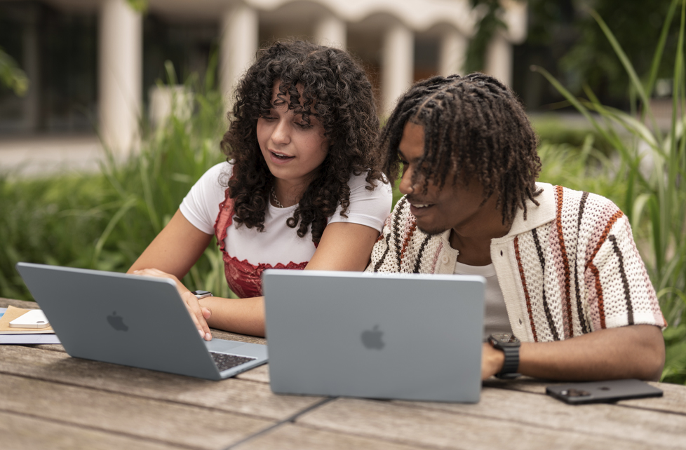 Two students using MacBook Air laptops while sitting at a table outside